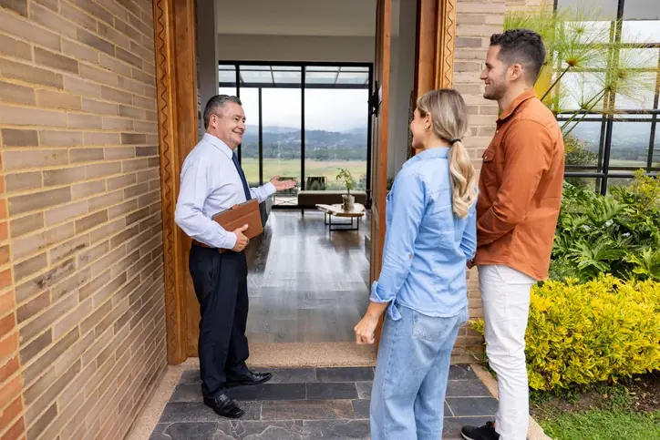 Con OIKOS Inmobiliaria, tu compra está en buenas manos Agente inmobiliario mostrando una casa a una pareja